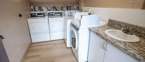 A compact laundry room with a washing machine, dryer, and a sink with granite countertop.