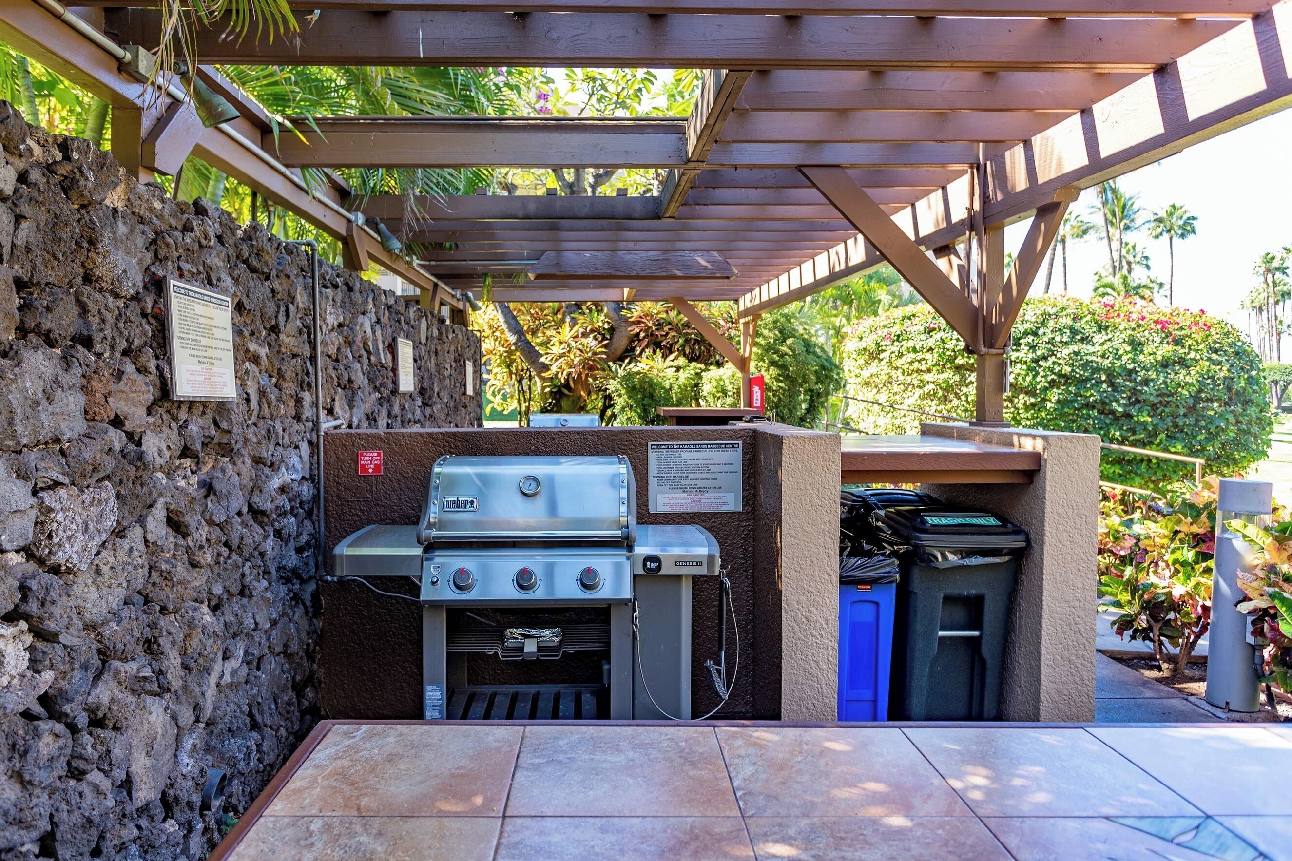 An outdoor barbecue area with a stone wall, a grill, and a covered seating area.