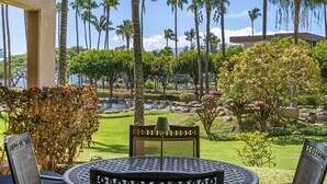 Un patio con una mesa redonda y sillas, rodeado de palmeras y un jardín ajardinado con un estanque.