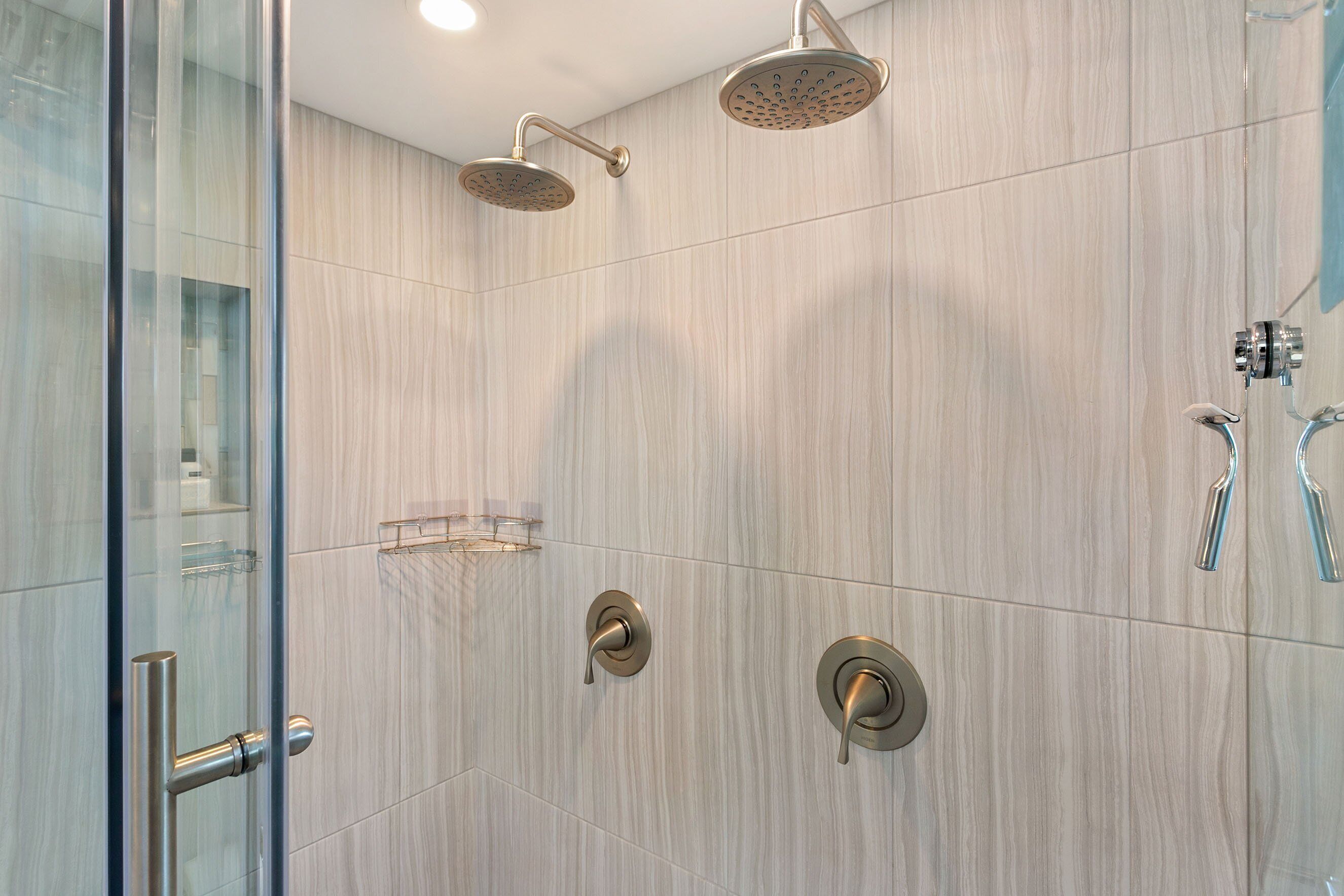 A modern shower area with a glass door, a wall-mounted showerhead, and a handheld showerhead.