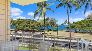 A balcony with a view of the ocean, palm trees, and a road with vehicles. - Haleakala Shores A-301 - Golden Sand Beaches, Ocean Views, Sleeps 6, Split AC! (Kihei)