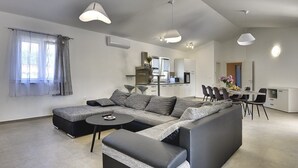 Una sala de estar moderna con un sofá modular, una mesita redonda y un comedor con una mesa y sillas blancas.