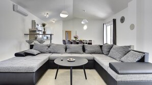 Una sala de estar moderna con un sofá modular, una mesa de centro redonda y una zona de cocina al fondo.