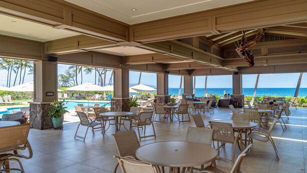 A covered outdoor area with tables and chairs, a pool, and a view of the ocean. - Wailea Ekahi 20J - Secluded Garden Oasis Surrounded by Trees & Tropical Blooms (Kihei)