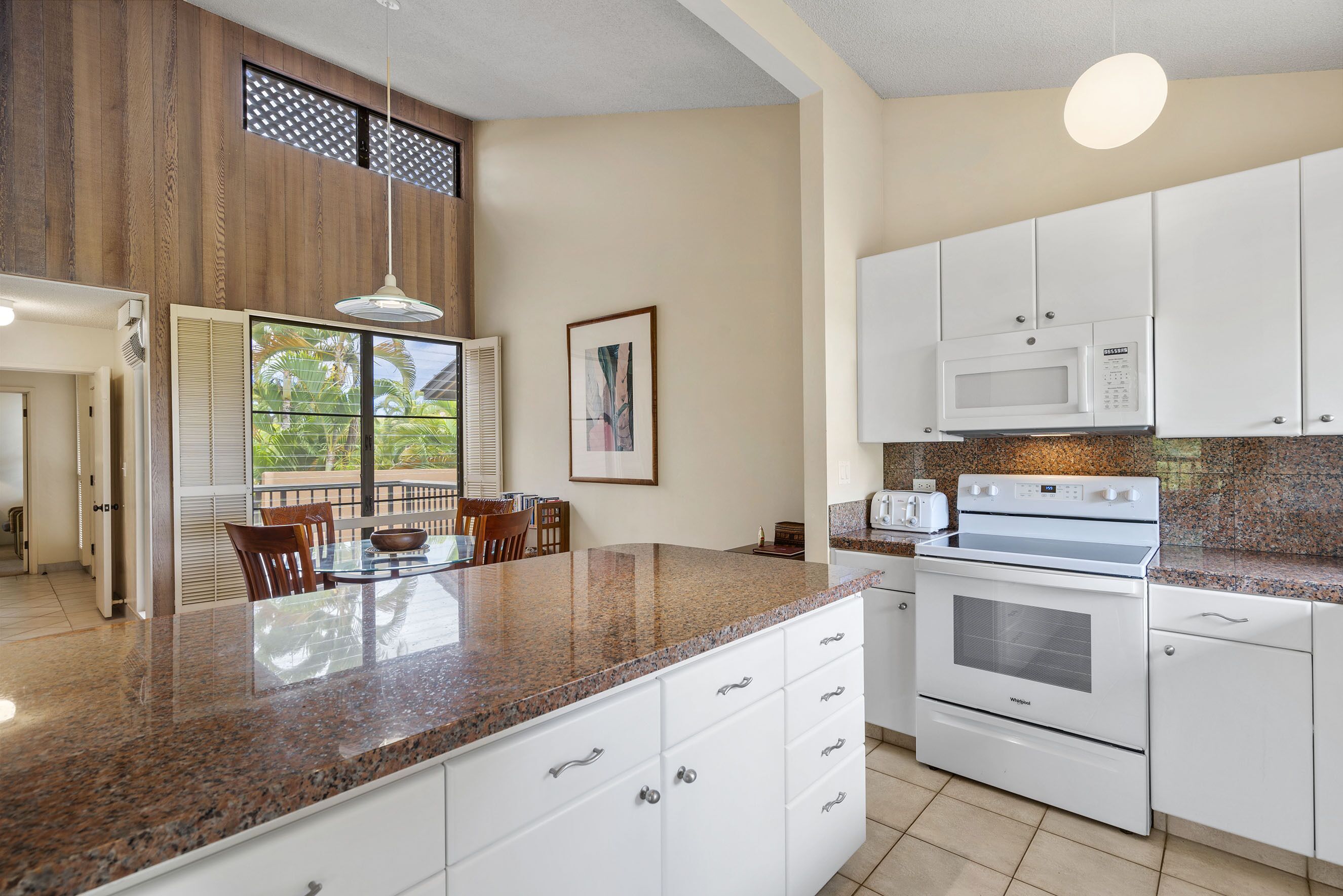 A modern kitchen with white cabinets, a granite countertop, a built-in oven, and a microwave.