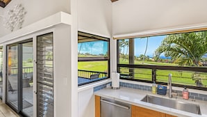 A modern kitchen with a large window, a stainless steel sink, and a view of a green landscape. - Wailea Ekolu 1204 - Modern Ocean View Condo w/ Large Lanai, King Bed, & Split AC (Kihei)