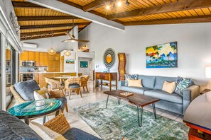 A modern living room with a sofa, chairs, a coffee table, and a dining area with a kitchen in the background. - Wailea Ekolu 1204 - Modern Ocean View Condo w/ Large Lanai, King Bed, & Split AC (Kihei)