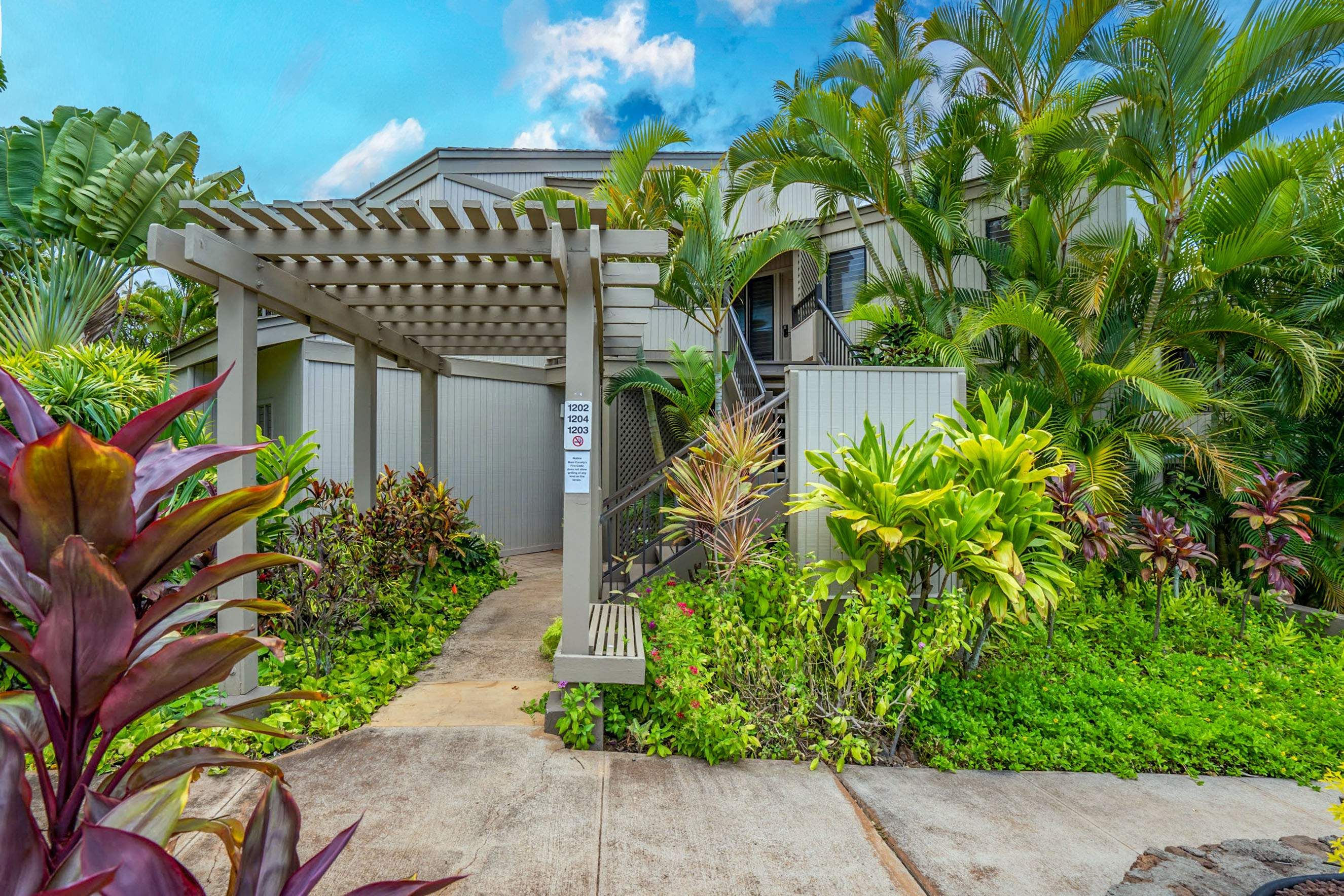 A gated entrance with a pergola, lush greenery, and a building with multiple windows.