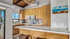 A modern kitchen with wooden cabinets, a large island, and pendant lighting. - Wailea Ekolu 1204 - Modern Ocean View Condo w/ Large Lanai, King Bed, & Split AC (Kihei)