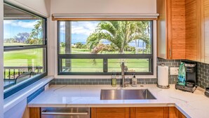 A kitchen with a large window, a stainless steel sink, wooden cabinets, and a Keurig coffee maker. - Wailea Ekolu 1204 - Modern Ocean View Condo w/ Large Lanai, King Bed, & Split AC (Kihei)
