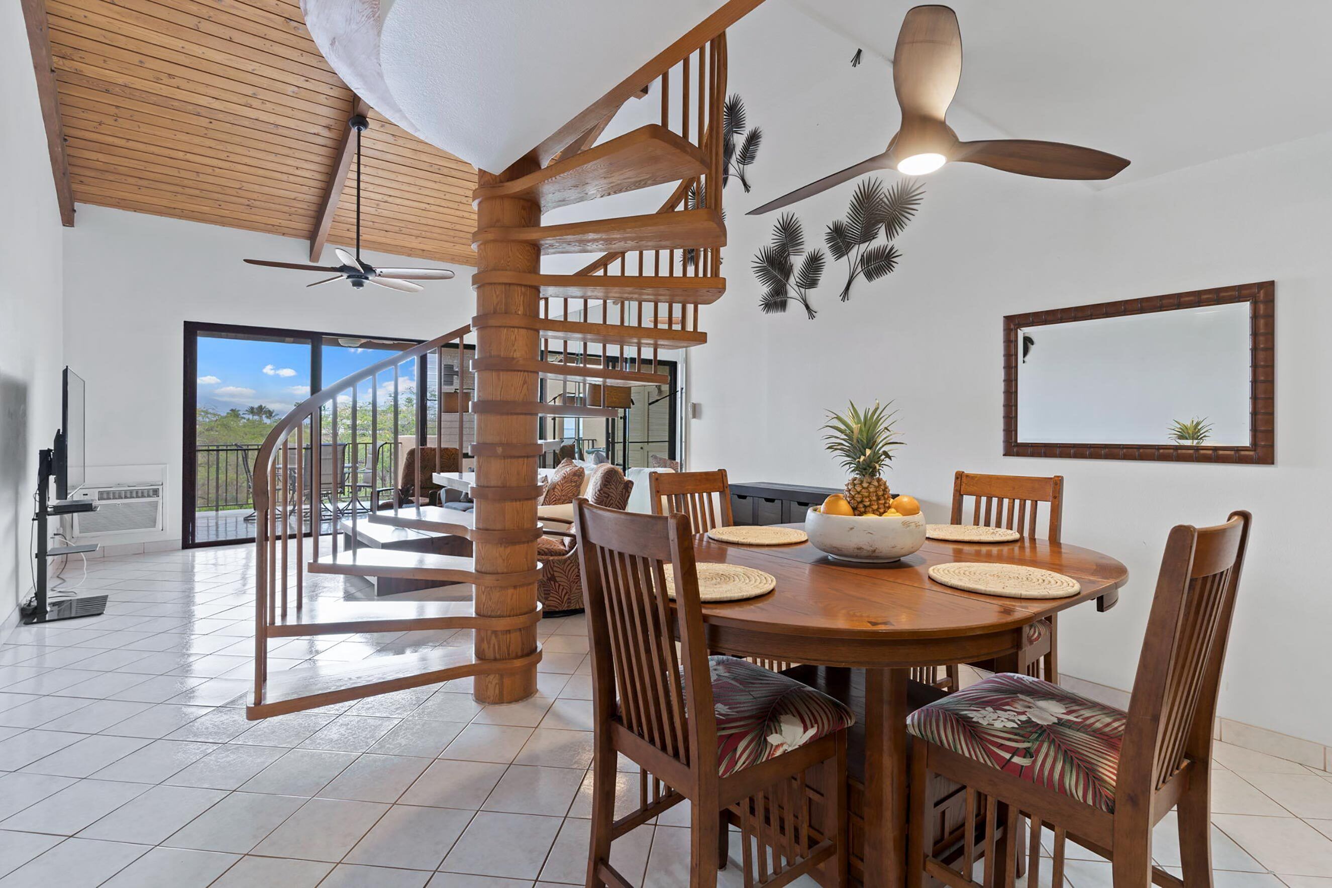 A spacious dining area with a wooden table and chairs, a spiral staircase, and a large window offering a view of the outdoors.