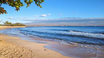 A beach with clear blue water, sandy shore, and distant mountains.
