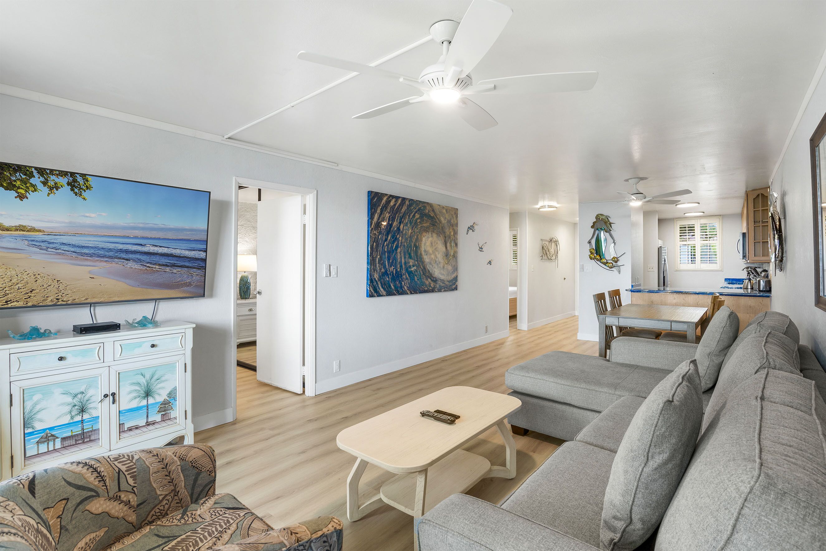 A spacious living area with a large flat-screen TV, a ceiling fan, and a dining area with a wooden table and chairs.
