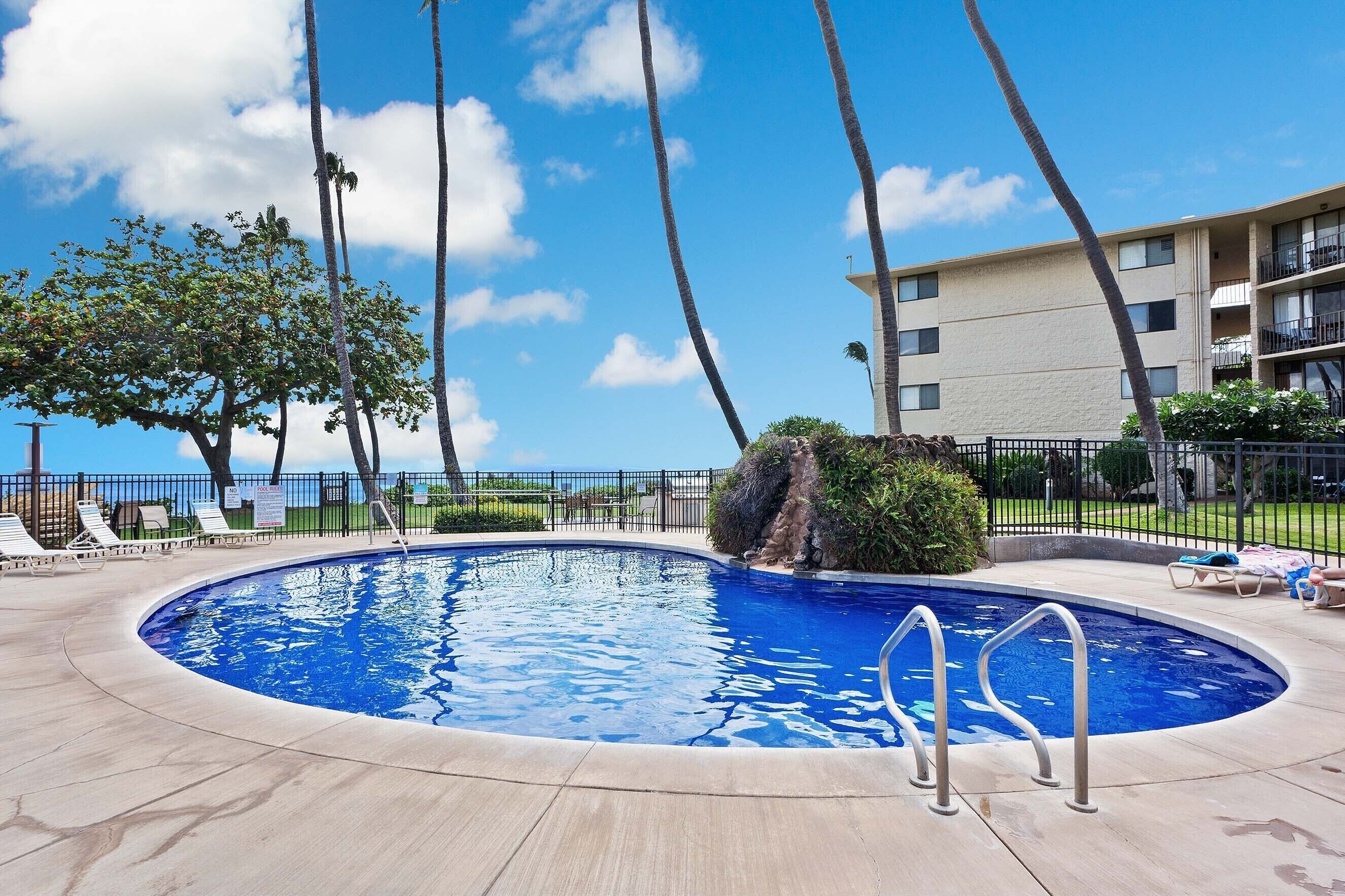 A swimming pool with a curved edge, surrounded by lounge chairs and a fence.