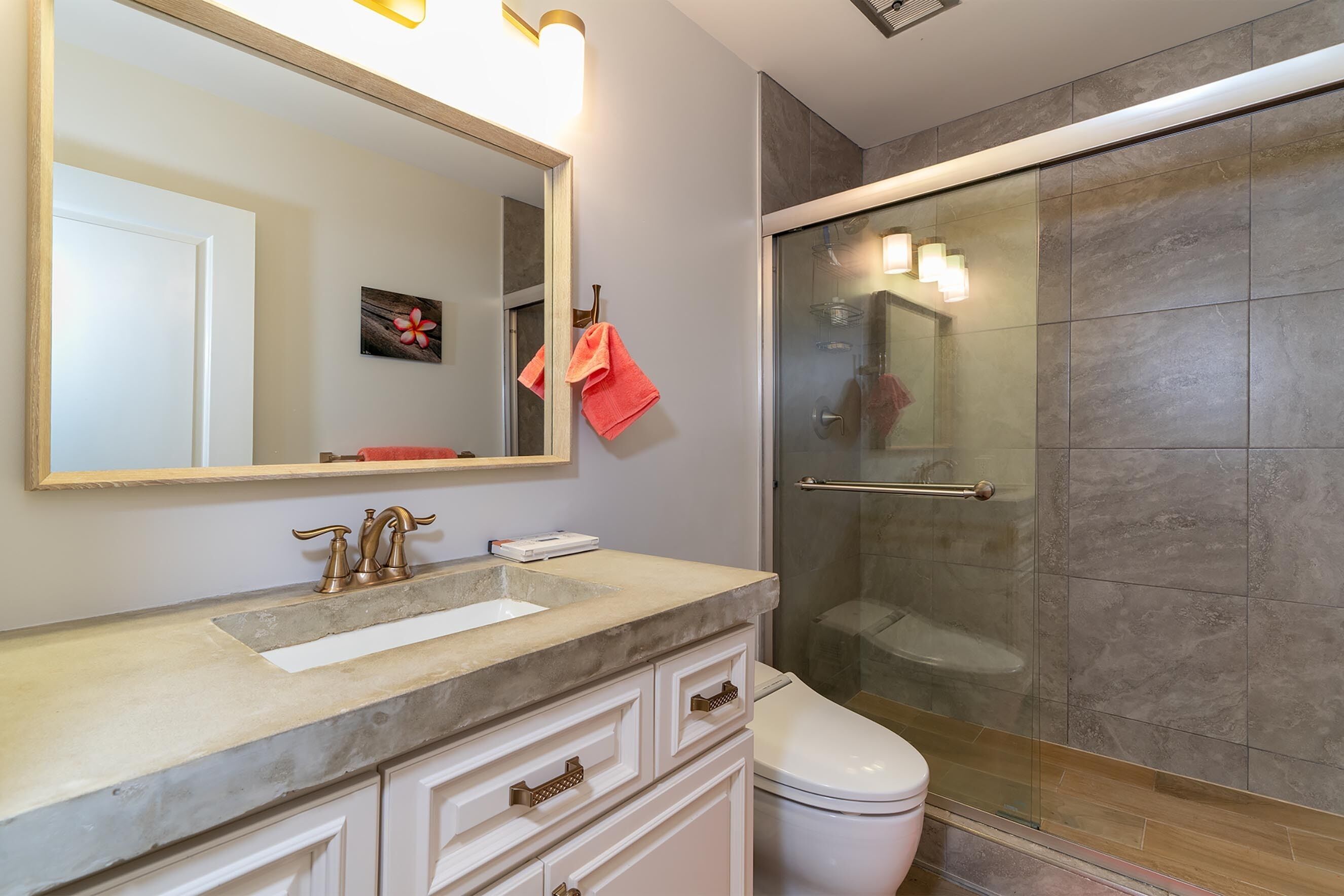 A bathroom with a large mirror, a sink, a toilet, and a glass-enclosed shower.