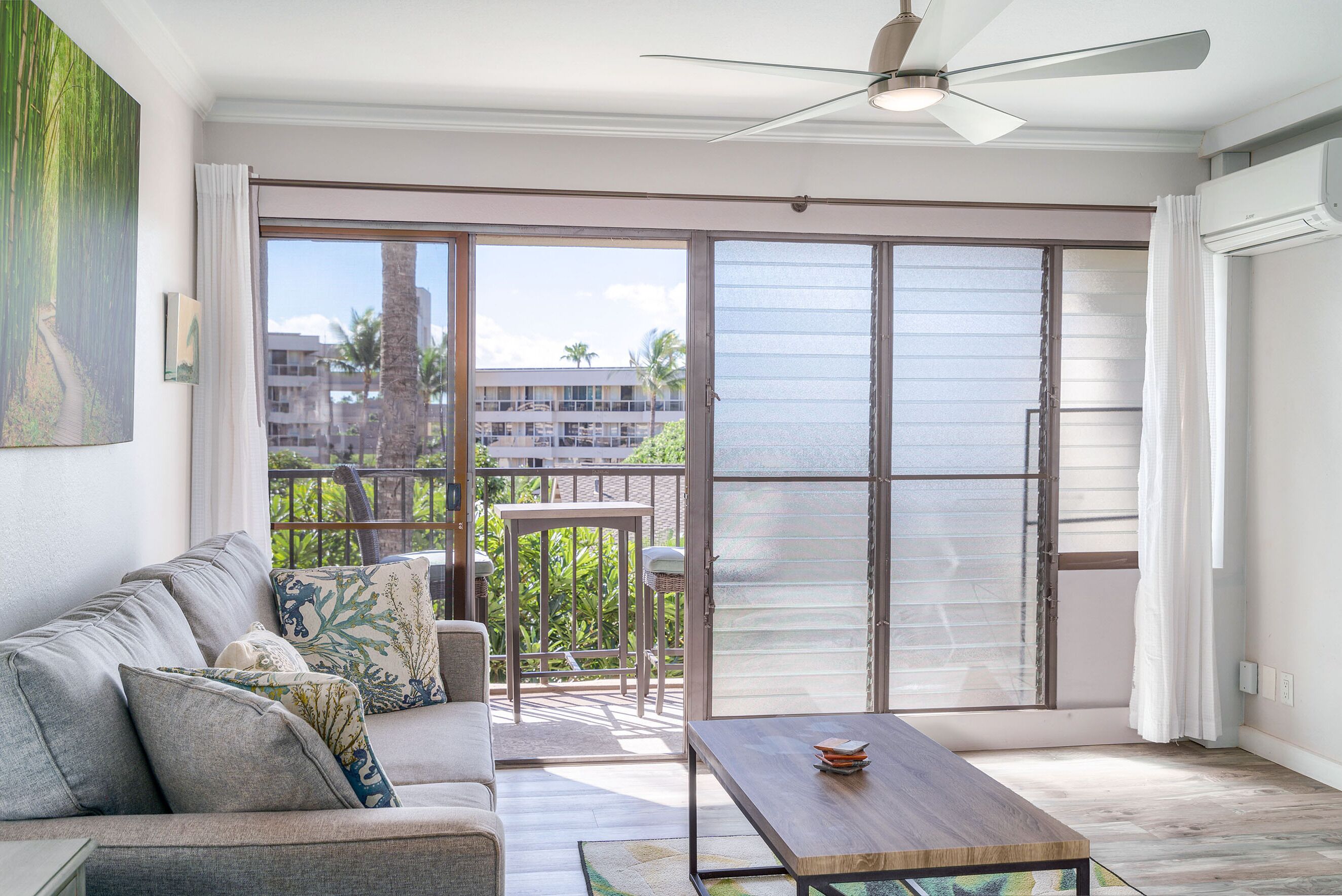 Un salon moderne avec un canapé, une table basse et une vue sur un balcon, accessible par de grandes portes-fenêtres coulissantes.