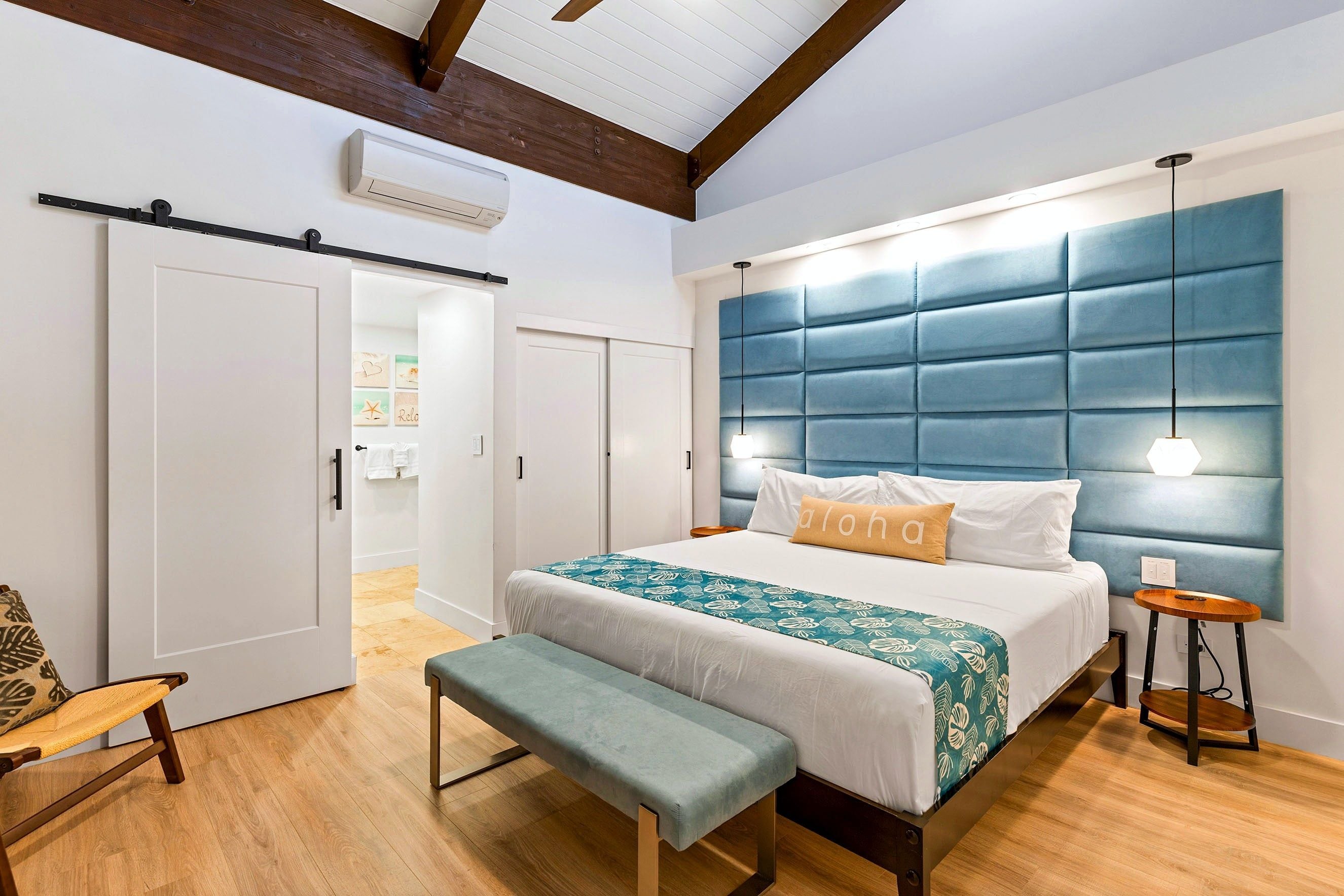 A bedroom with a large bed, a bench, a bedside table, and a hanging light fixture.