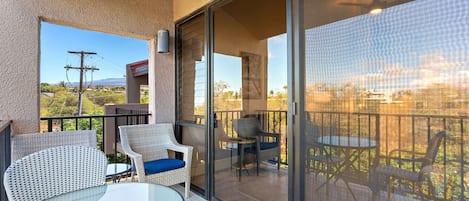 Un balcón con mobiliario de mimbre, una mesa de vidrio y vistas del paisaje circundante.