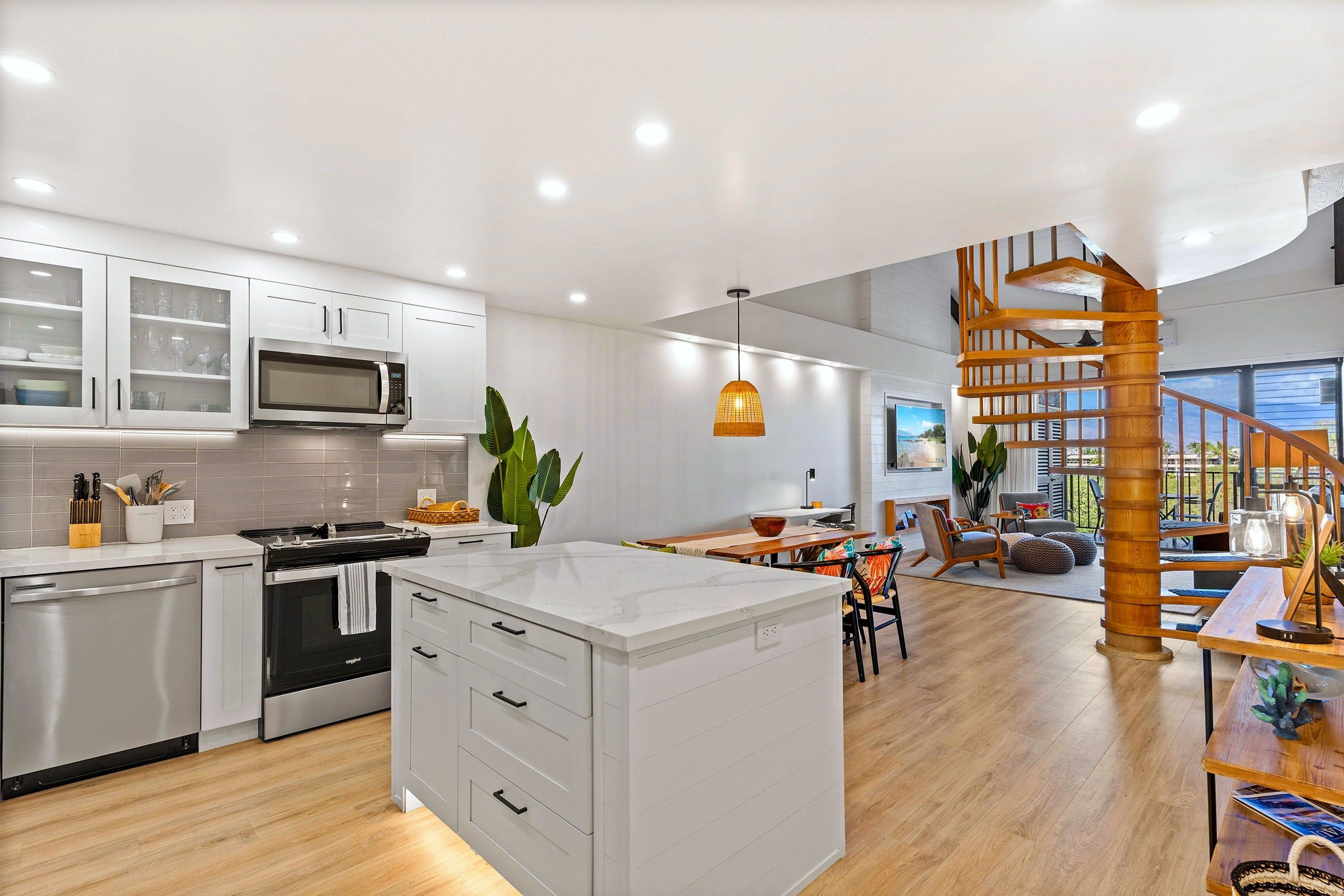 Cocina moderna con armarios blancos, una isla central y un comedor con una escalera de madera.