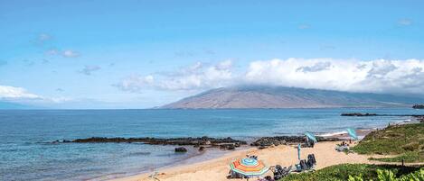 Une plage offrant une vue dégagée sur l’océan, une montagne à l’horizon et une côte rocheuse.