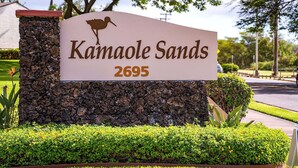 A sign for Kamaole Sands with the address 2695, set against a backdrop of landscaped greenery and trees. - Summer Sale! Deluxe Modern Renovation, Split-ac, Kamaole Sands 4-411, Book Now! (Kihei)