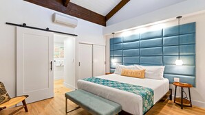 A bedroom with a large bed, a bench, a bedside table, and a hanging light fixture. - Summer Sale! Deluxe Modern Renovation, Split-ac, Kamaole Sands 4-411, Book Now! (Kihei)