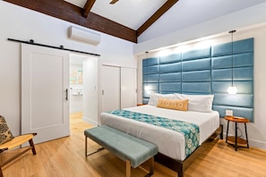 A bedroom with a large bed, a bench, a bedside table, and a hanging light fixture.