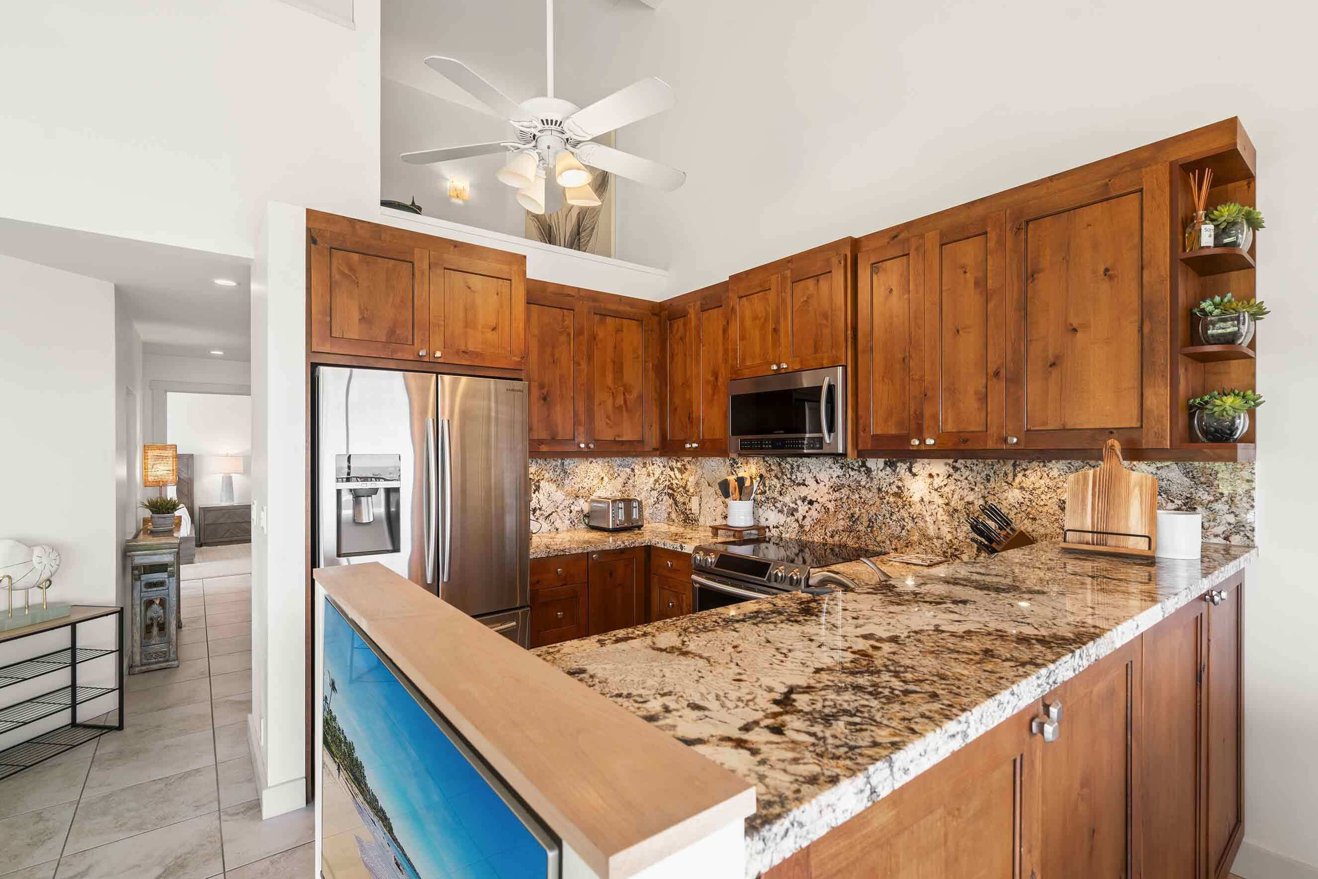 A kitchen with wooden cabinets, granite countertops, stainless steel appliances, and a ceiling fan.