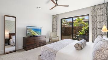 A bedroom with a bed, a television, a ceiling fan, a chair, and a view of the outdoors.