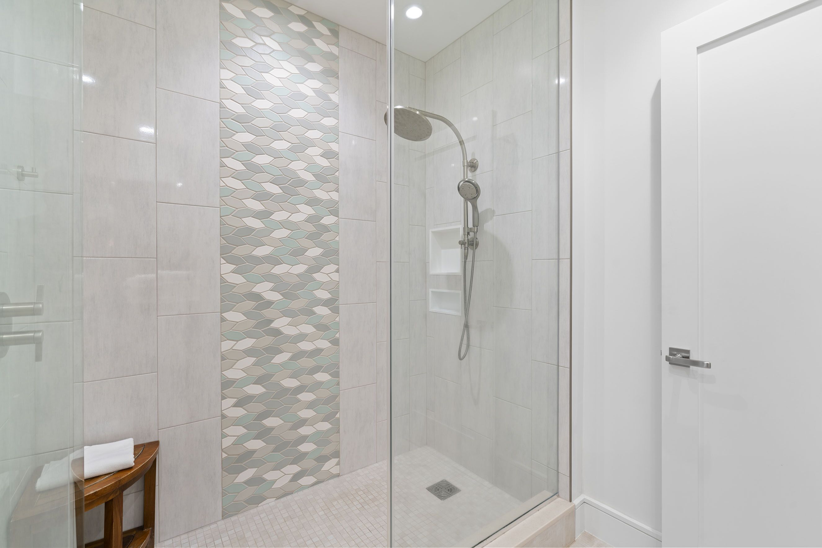 Un espace douche moderne doté d’une porte en verre, de murs carrelés et d’un pare-douche décoratif.