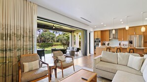 A modern living room with a sofa, chairs, and a coffee table. There is a kitchen area with cabinets and appliances. The room has large windows and a view of greenery outside. - New Listing! Honua Kai Luana Garden Villas 7B - Ground Level, Private Lanai, BBQ (Lahaina)