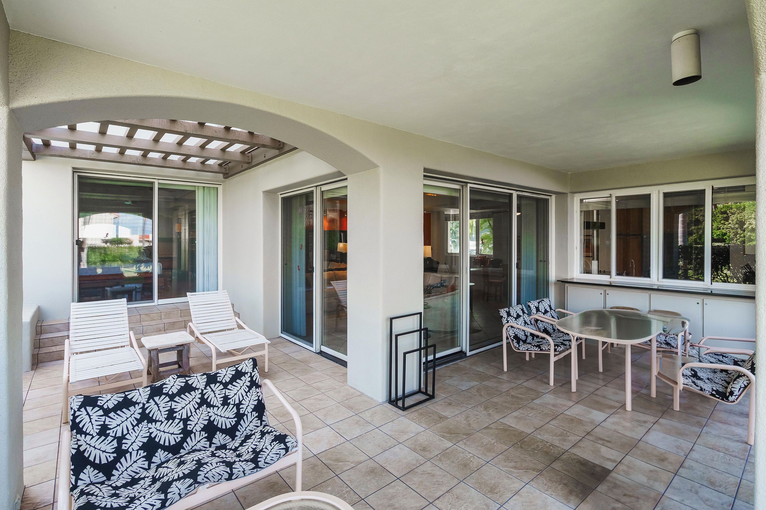 A covered patio area with a seating arrangement, including a table and chairs, and a sofa.