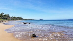 Ein Strand mit klarem, blauem Wasser, sandigem Ufer und bewaldetem Hintergrund.