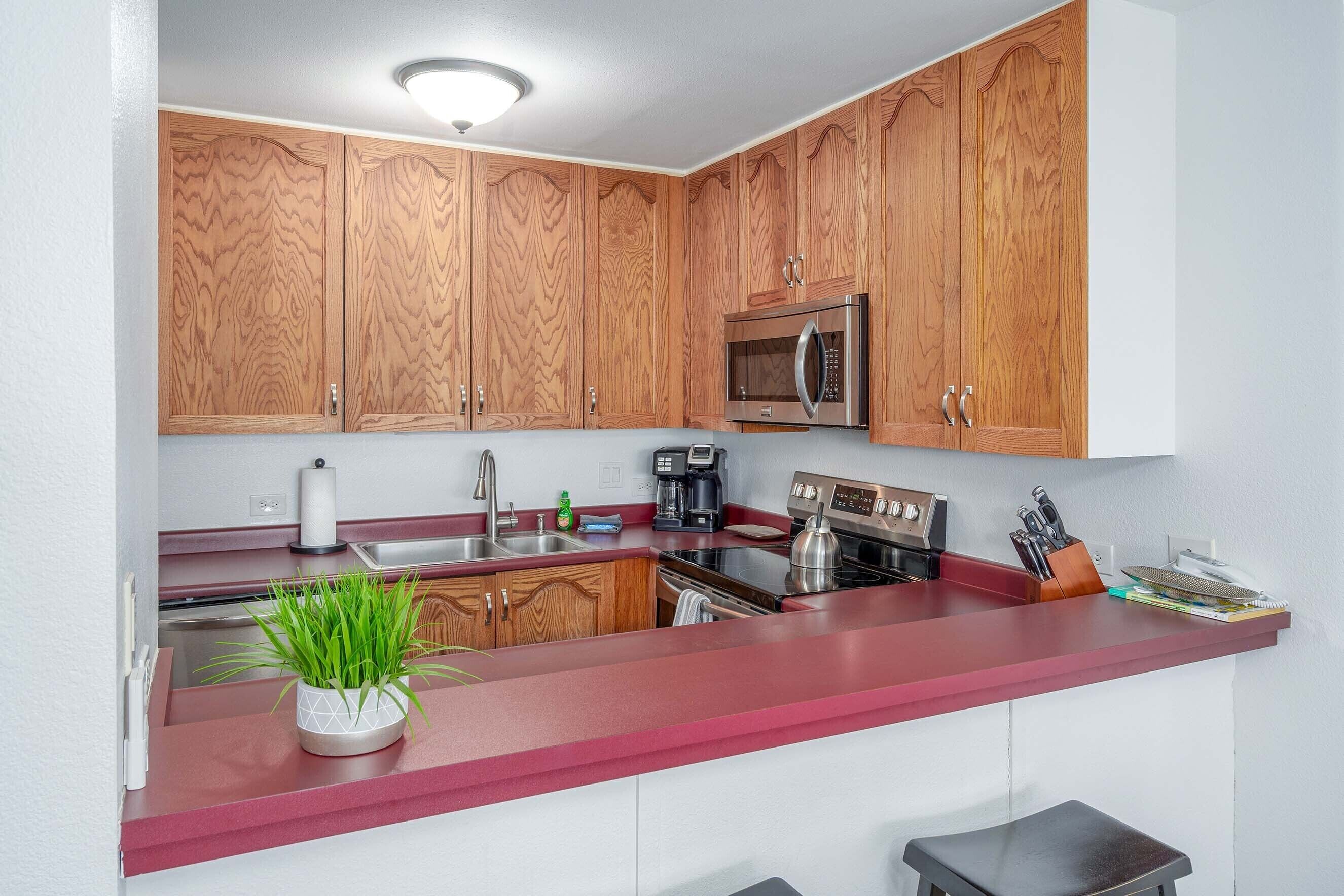 Una cocina con armarios de madera, microondas, lavamanos y encimera con una planta.