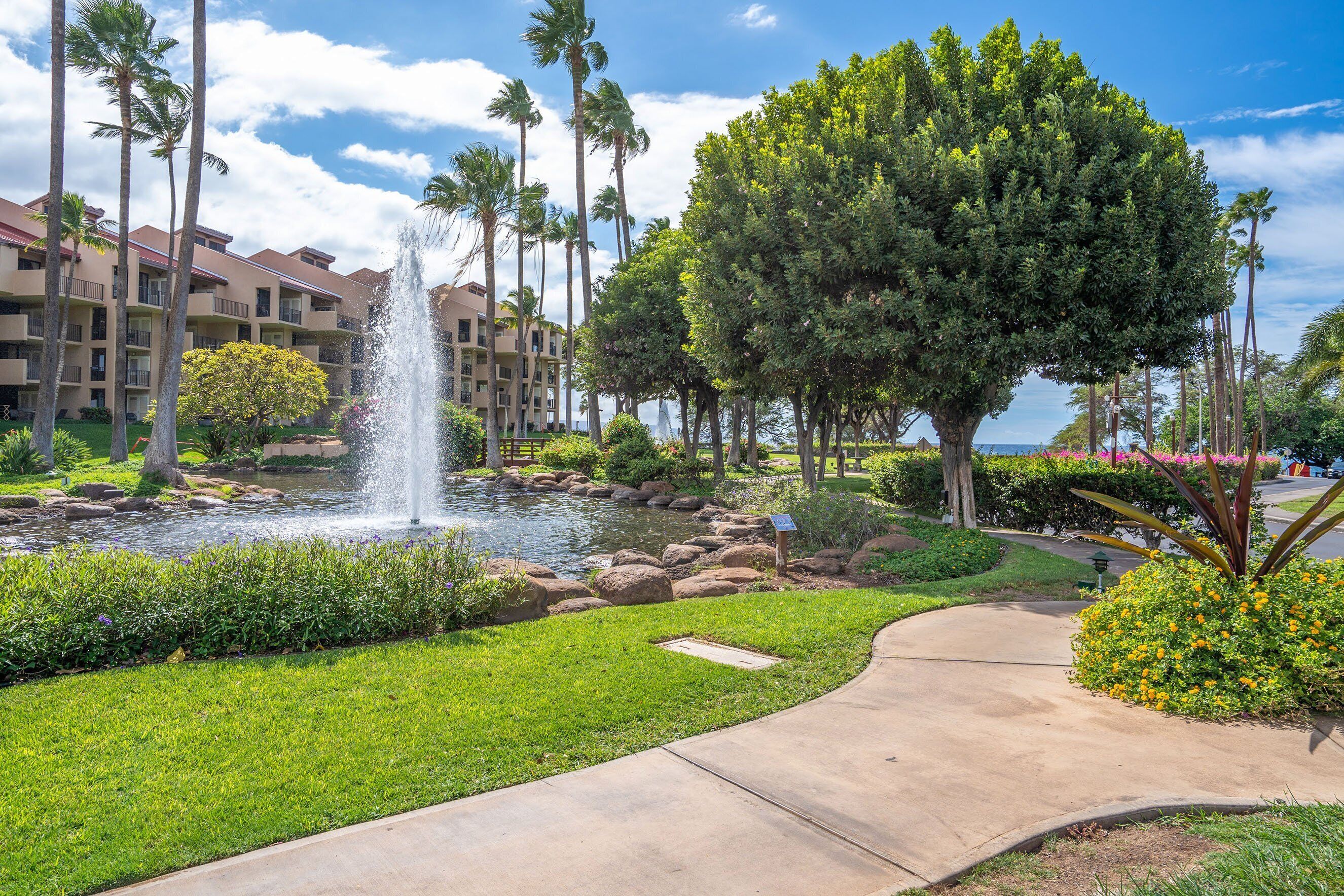 A landscaped area with a fountain, palm trees, and a building with balconies.