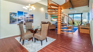 Uma sala ampla com uma escada espiral de madeira, uma mesa de jantar com cadeiras de vime e uma grande janela com vista para o exterior.