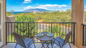 Varanda com duas cadeiras e uma mesa, com vista para uma estrada e uma montanha.