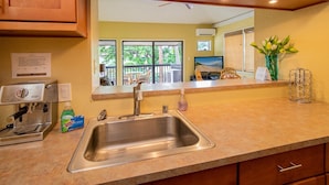 A kitchen with a stainless steel sink, a coffee machine, and a view of a balcony with outdoor furniture. - Kihei Garden Estates C-201, Ocean Views, Near the Beach, Renovated, w/ Split AC! (Kihei)
