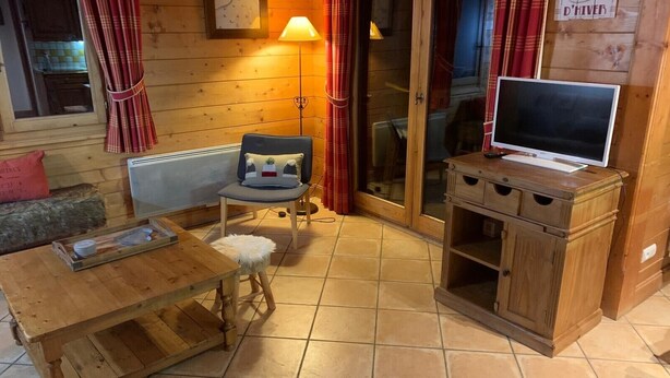 Une pièce chaleureuse avec un décor intérieur en bois, un téléviseur posé sur un meuble en bois, un fauteuil avec un coussin et une table avec un plateau.
