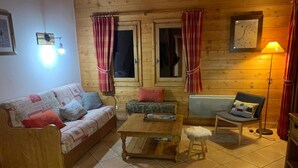L’intérieur d’un chalet accueillant, avec un plancher en bois, un canapé, un fauteuil, une petite table et une lampe.