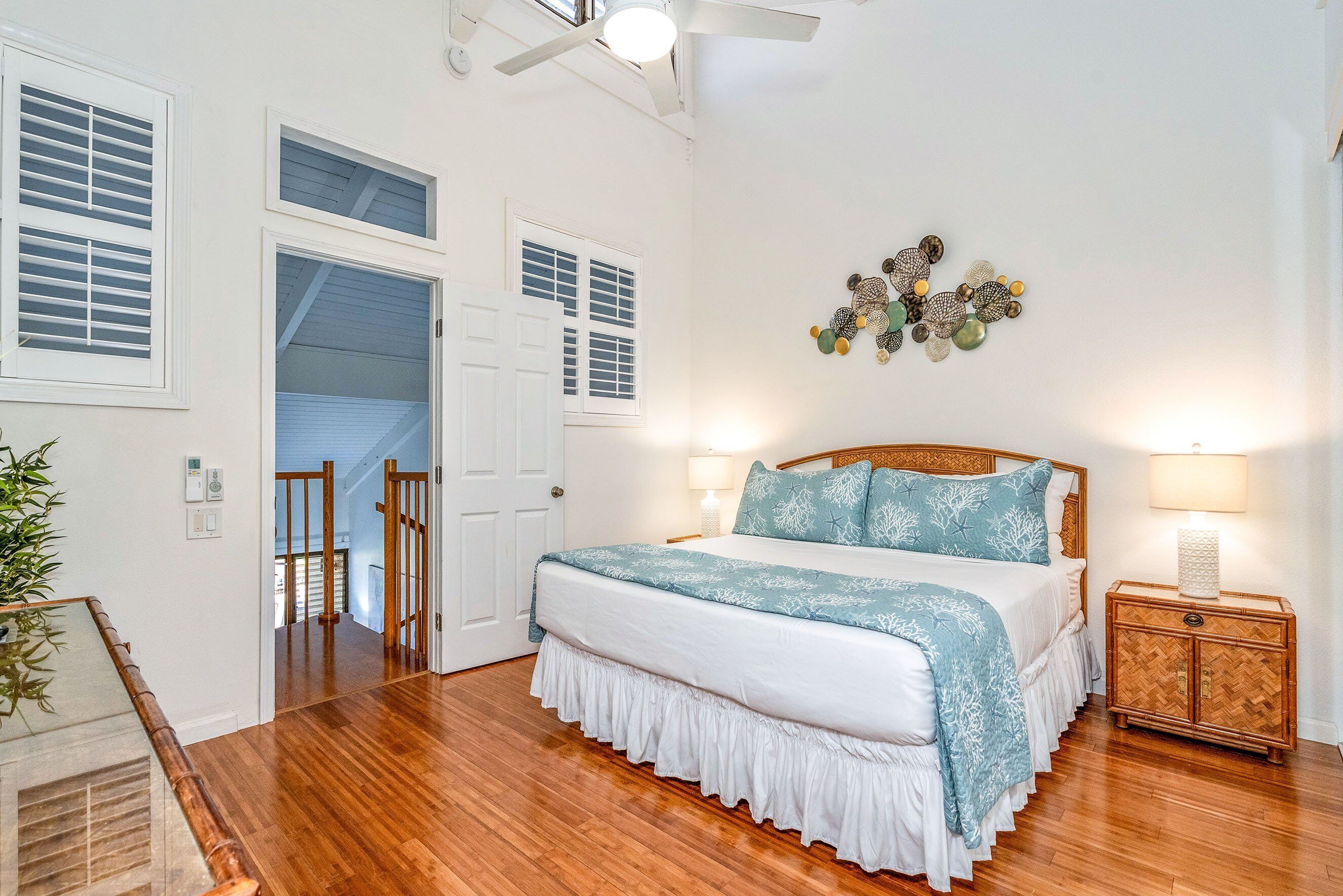 A bedroom with a wooden floor, a bed with a white and blue bedspread, two bedside lamps, a decorative wall piece, and a small wooden nightstand.