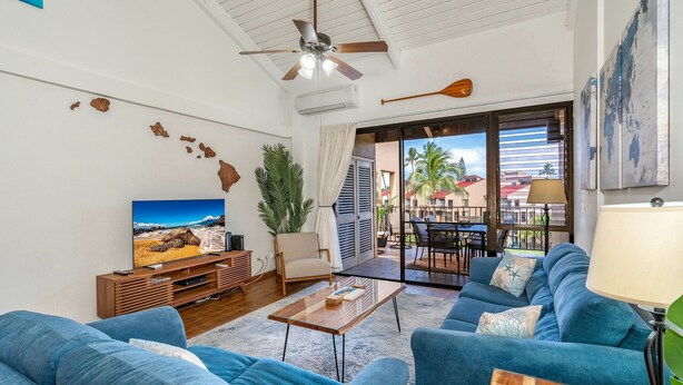 A living room with a TV, sofas, a coffee table, and a ceiling fan. - Kamaole Sands 7-405 - Stunning Renovation, Large Lanai, Ocean Views, Split AC! (Kihei)