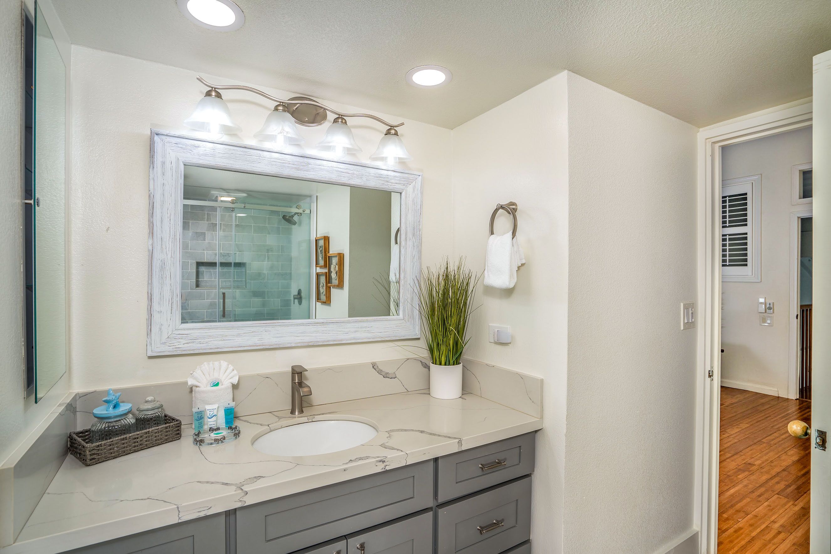 A bathroom with a white marble sink, a large mirror with three lights, and a potted plant.