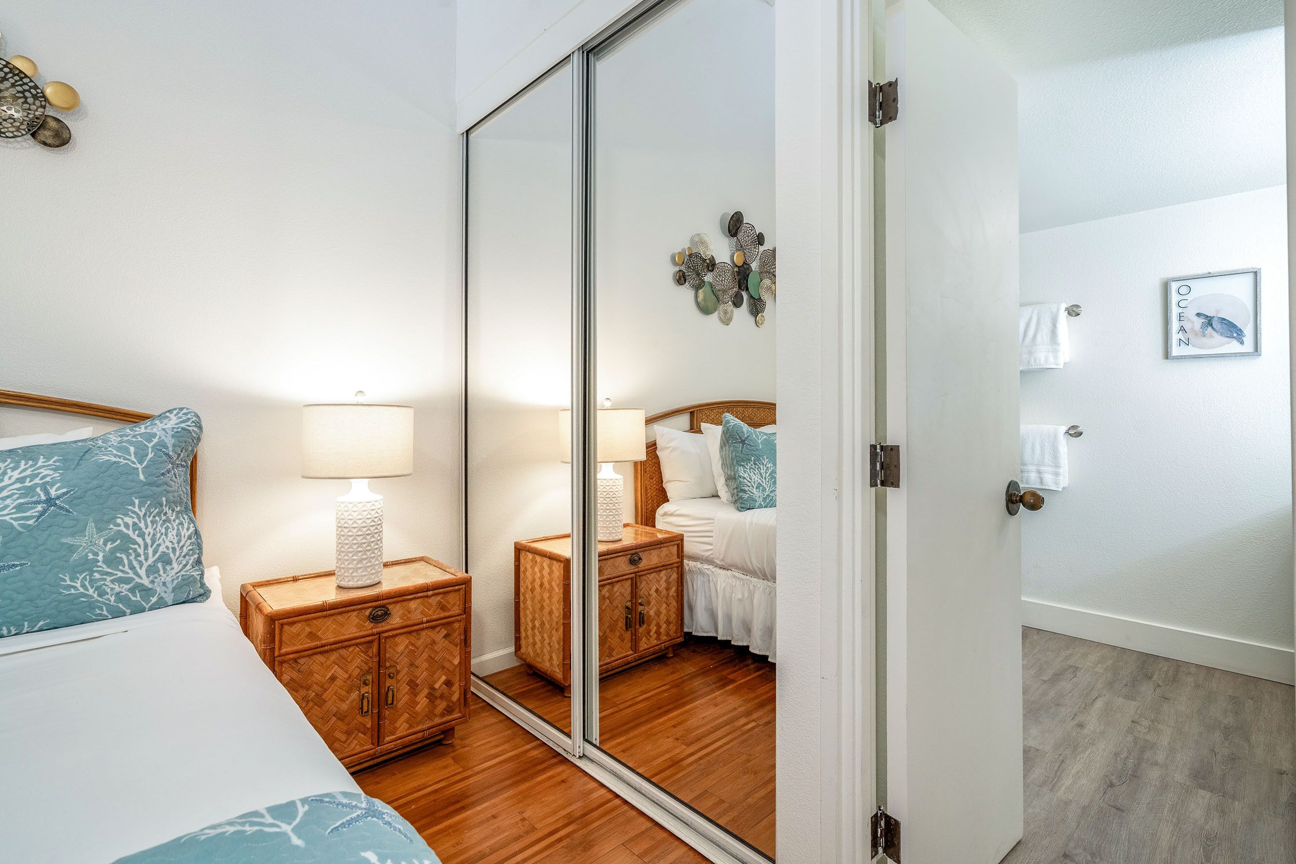 Un dormitorio con cama, mesitas de noche, un espejo y una puerta que da a otra habitación.