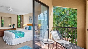 Een hotelkamer met balkon, een bed met wit- en blauwe spreideken, een klein tafeltje en een stoel.