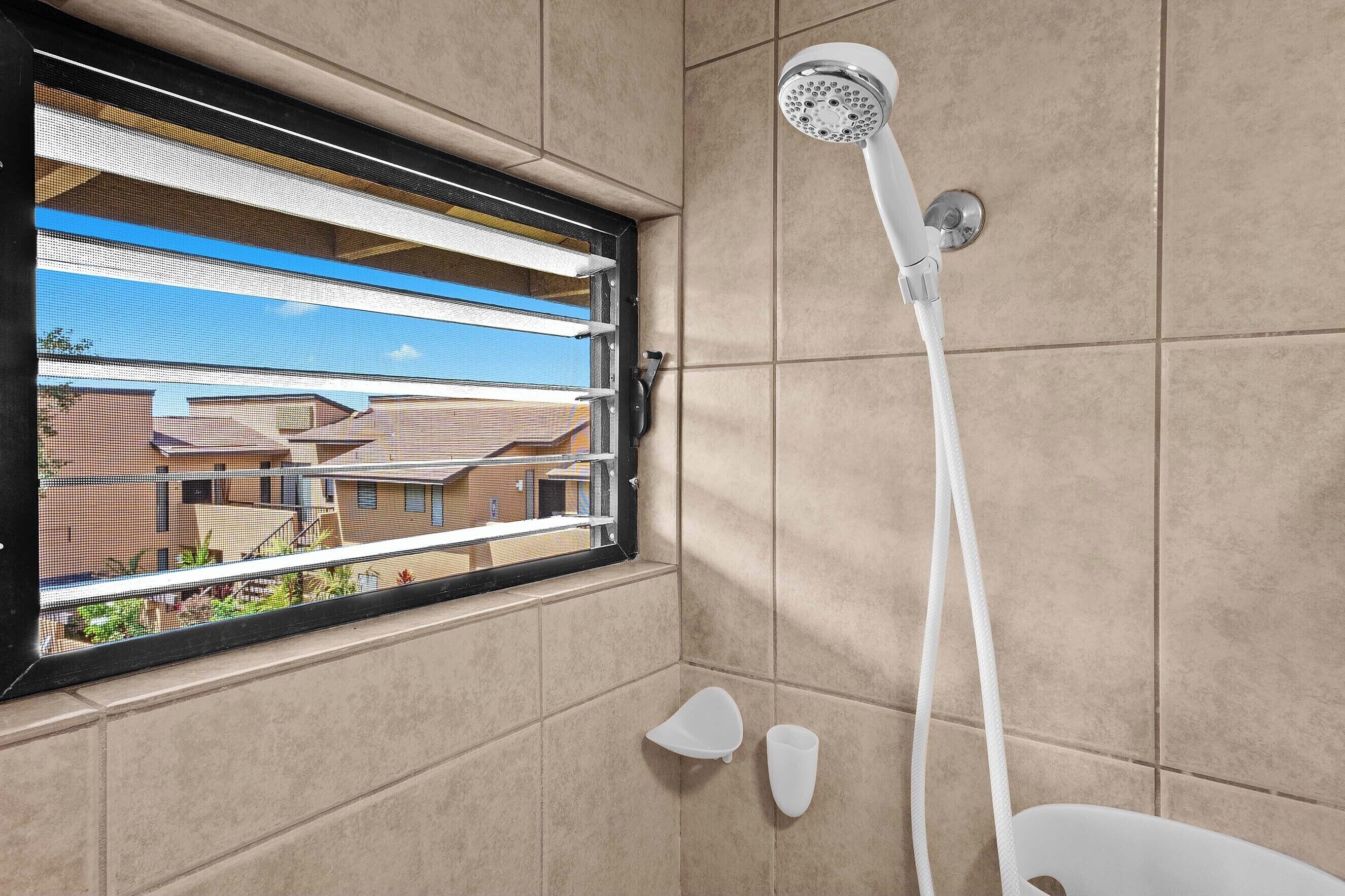 A shower with a window, a view of houses, and a tiled wall.