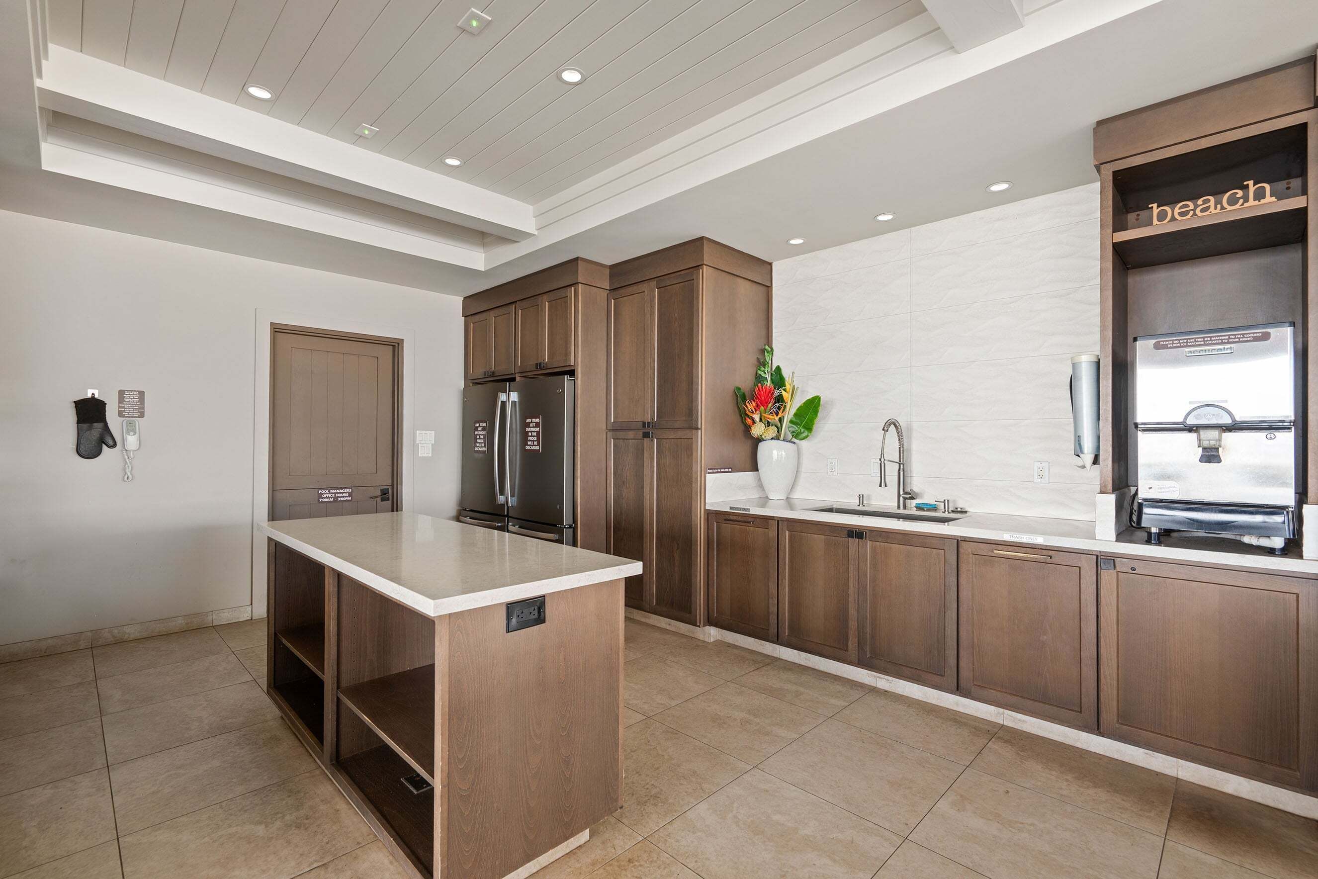 Une cuisine moderne avec des meubles en bois, un îlot central, des appareils électroménagers en acier inoxydable et un panneau décoratif représentant une plage accroché au mur.