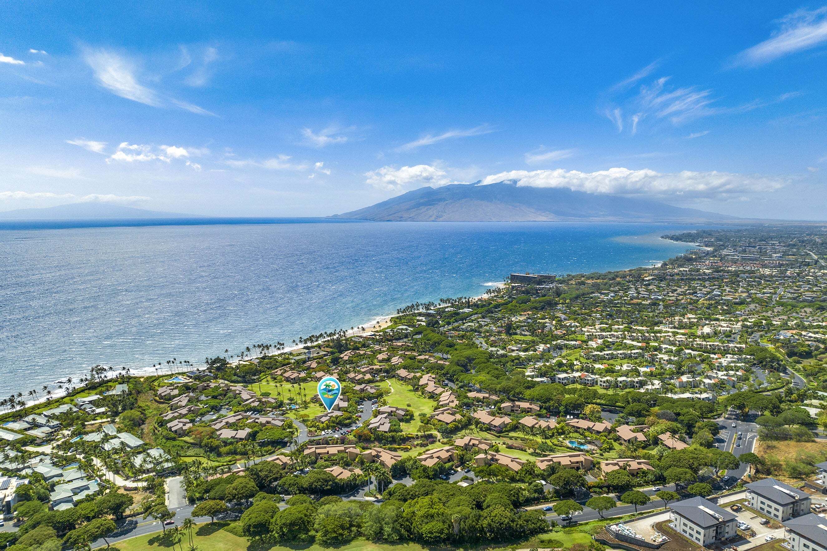 Vue aérienne d’une zone résidentielle côtière, avec des maisons, une plage et une montagne en arrière-plan.
