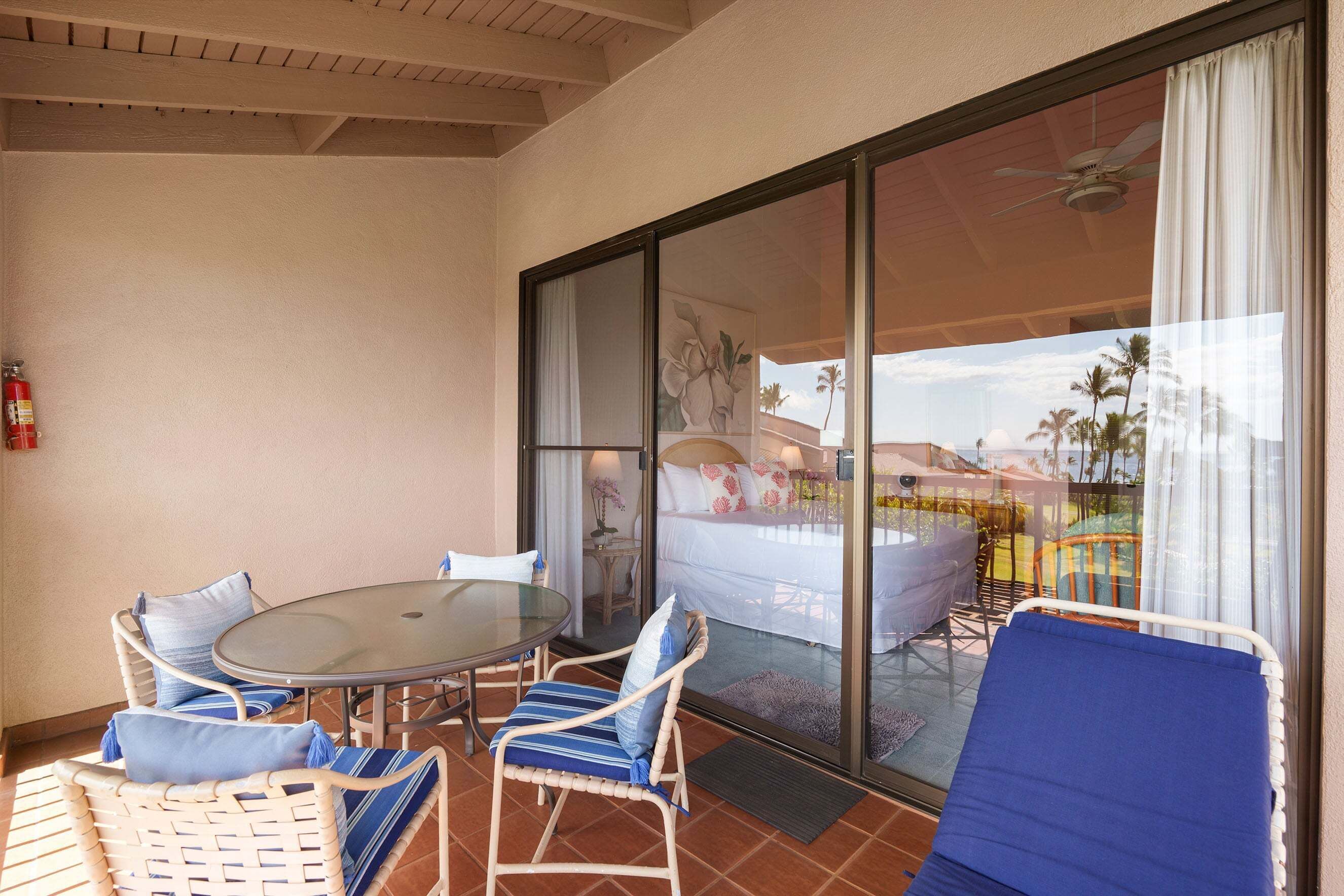 A balcony with a glass door, wicker chairs, a round table, and a bed with a view.