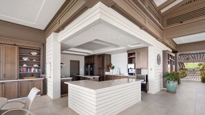 A modern kitchen with a central island, wooden cabinetry, and a dining area with a chair. - Wailea Ekahi 12D - Budget Friendly Ocean View Studio w/ Lanai, Kitchen, WD, & AC (Kihei)